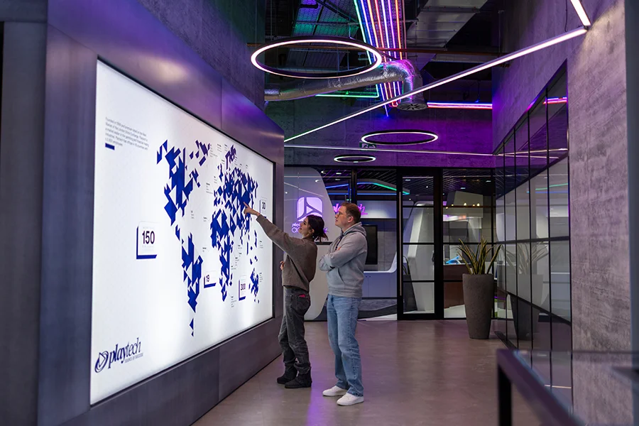 Two colleagues in the Playtech office reviewing a wall display.